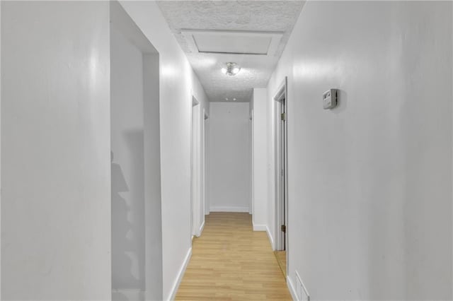 hall with light wood finished floors, attic access, visible vents, baseboards, and a textured ceiling