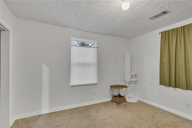 unfurnished room with light carpet, baseboards, visible vents, and a textured ceiling