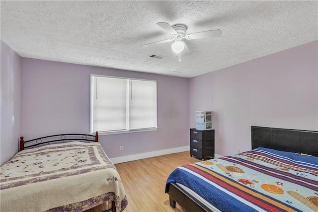 bedroom with visible vents, light wood-style flooring, a ceiling fan, a textured ceiling, and baseboards