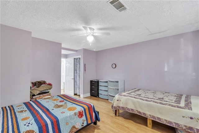 bedroom featuring a textured ceiling, wood finished floors, visible vents, a ceiling fan, and a closet