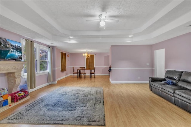 living room with baseboards, wood finished floors, a tray ceiling, a textured ceiling, and ceiling fan with notable chandelier