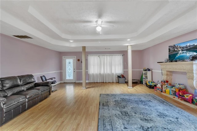 living room with visible vents, a textured ceiling, a tray ceiling, and wood finished floors