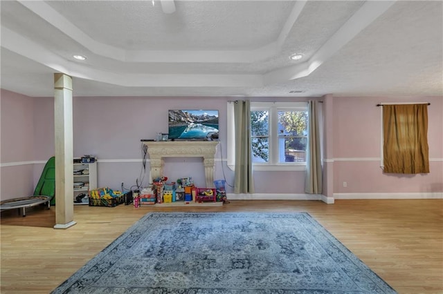 recreation room with a textured ceiling, baseboards, a raised ceiling, and wood finished floors