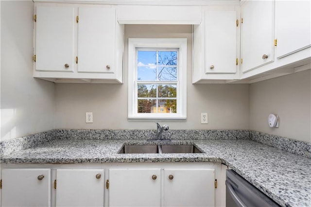 kitchen with light stone counters, white cabinetry, stainless steel dishwasher, and a sink