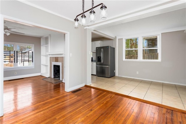 unfurnished living room featuring visible vents, baseboards, a tile fireplace, a ceiling fan, and wood-type flooring