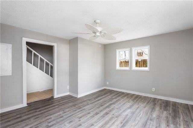 empty room with ceiling fan, stairway, baseboards, and wood finished floors