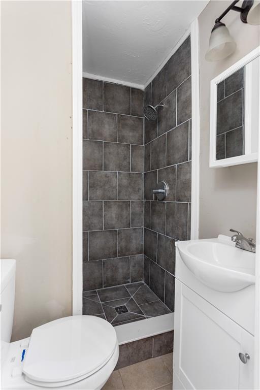 bathroom with tile patterned flooring, a stall shower, toilet, and vanity