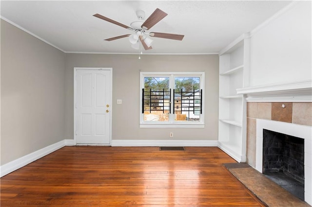 unfurnished living room featuring crown molding, wood finished floors, baseboards, and a tile fireplace