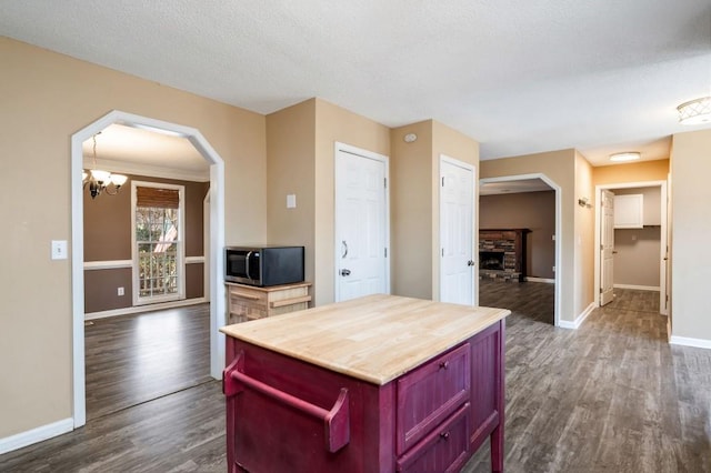 kitchen featuring butcher block countertops, an inviting chandelier, dark hardwood / wood-style floors, a fireplace, and a textured ceiling