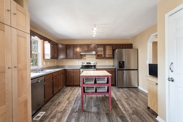 kitchen with glass insert cabinets, appliances with stainless steel finishes, light countertops, under cabinet range hood, and a sink