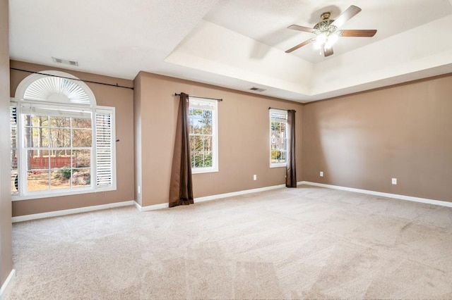 empty room featuring light colored carpet, a tray ceiling, visible vents, and baseboards