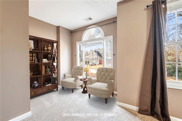 living area with light carpet, a textured ceiling, visible vents, and baseboards