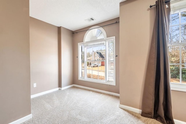 empty room featuring baseboards, a textured ceiling, visible vents, and light colored carpet