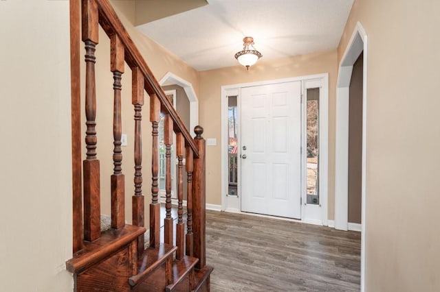 foyer entrance with dark wood-style floors, arched walkways, stairway, and baseboards