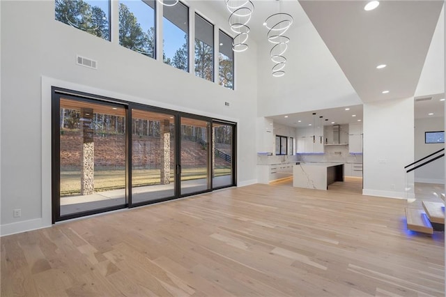 1678 Thomas Dr, Hoschton, GA 30548 - unfurnished living room with light wood finished floors, a towering ceiling, baseboards, a chandelier, and recessed lighting