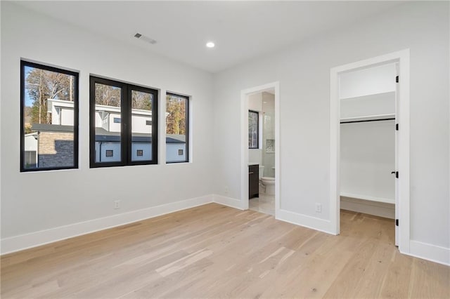 1678 Thomas Dr, Hoschton, GA 30548 - unfurnished bedroom with light wood-style flooring, multiple windows, a walk in closet, baseboards, and recessed lighting