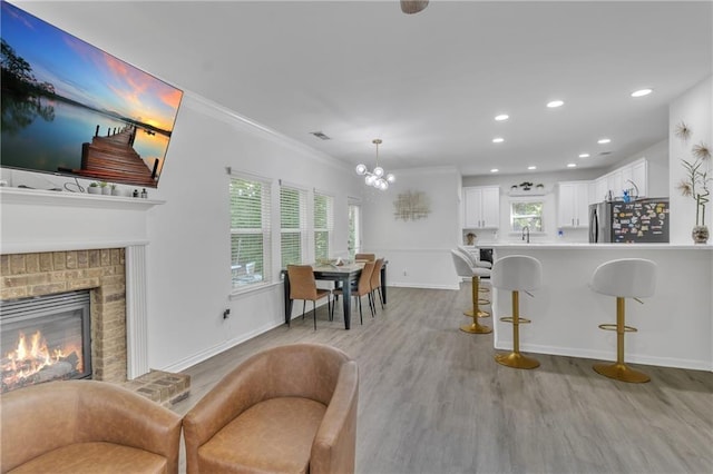 living room featuring light wood-type flooring, a chandelier, baseboards, a brick fireplace, and crown molding