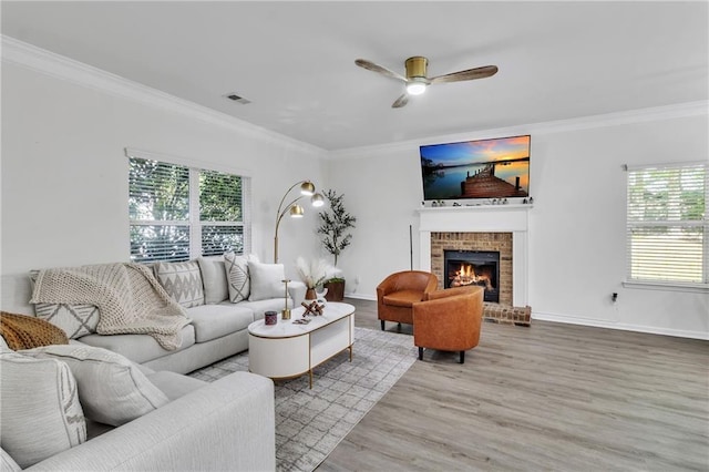 living room with ornamental molding, healthy amount of natural light, wood finished floors, ceiling fan, and a brick fireplace