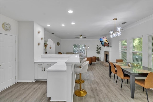 kitchen featuring ornamental molding, light wood-style flooring, a fireplace with raised hearth, a kitchen bar, and light countertops