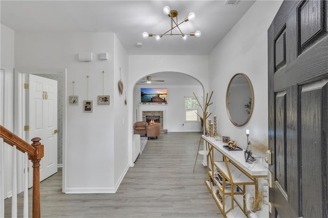 entryway featuring ceiling fan, a fireplace, wood finished floors, a chandelier, and arched walkways