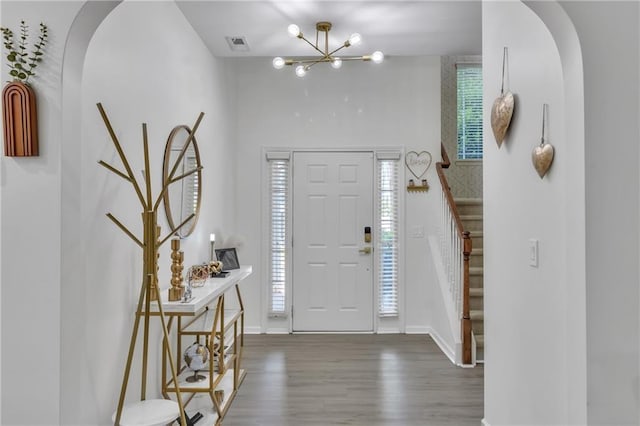 entrance foyer featuring wood finished floors, stairs, arched walkways, and a chandelier