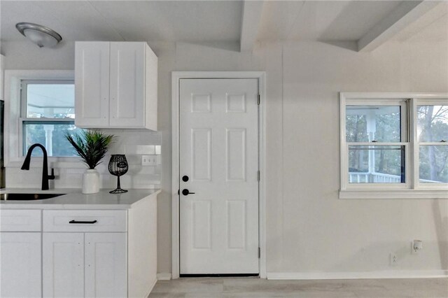 kitchen featuring white cabinetry, light countertops, a sink, baseboards, and beam ceiling