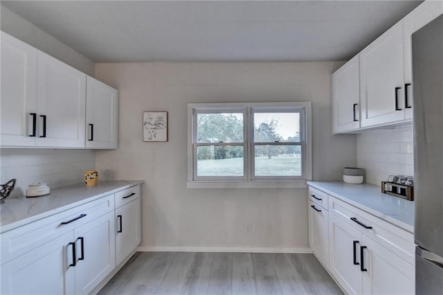 kitchen with light wood-type flooring, decorative backsplash, light countertops, and white cabinetry