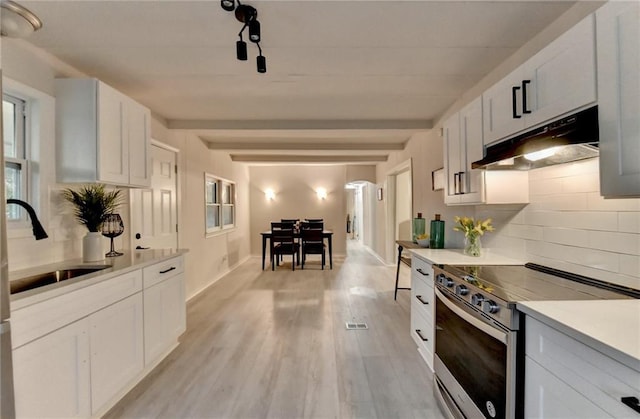 kitchen with tasteful backsplash, light countertops, under cabinet range hood, stainless steel range with electric cooktop, and a sink