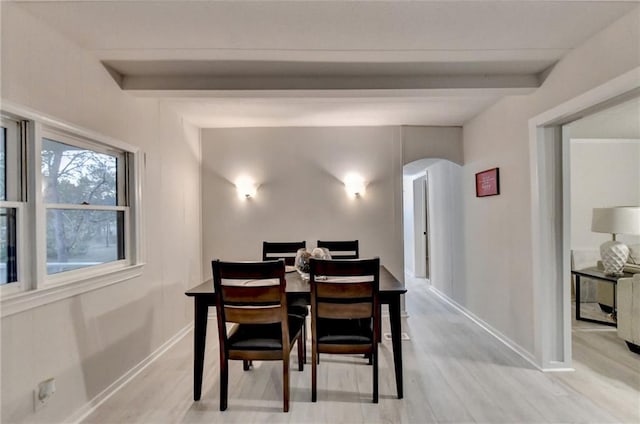 dining area featuring arched walkways, beamed ceiling, baseboards, and light wood-style floors