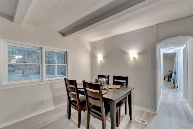 dining area featuring arched walkways, visible vents, beamed ceiling, and light wood-style flooring