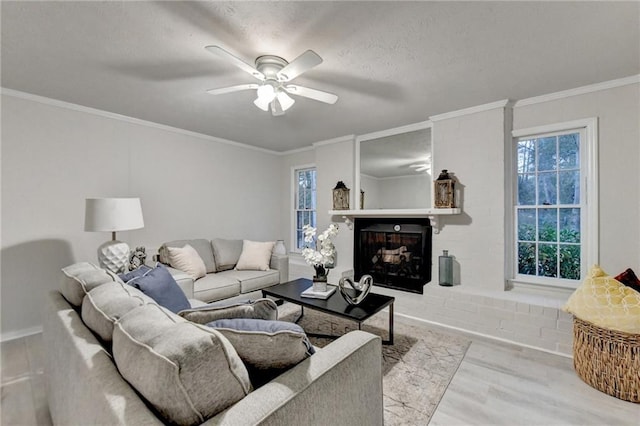 living area with ornamental molding, a fireplace, plenty of natural light, a ceiling fan, and wood finished floors