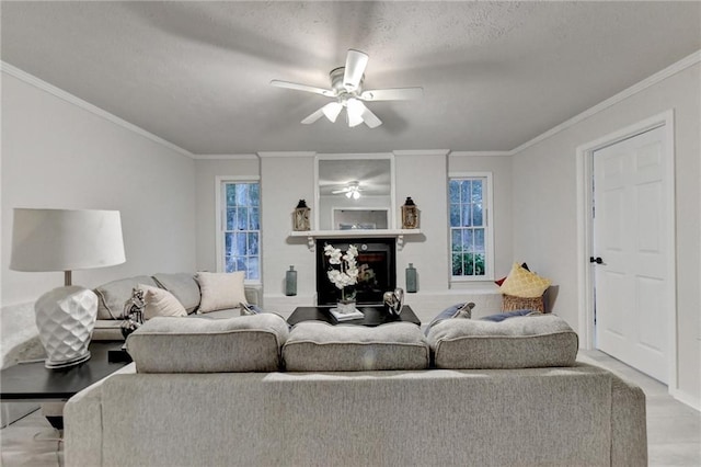 living area with a textured ceiling, ornamental molding, a ceiling fan, and a fireplace with raised hearth