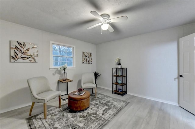 living area featuring light wood-type flooring, a textured ceiling, and ceiling fan