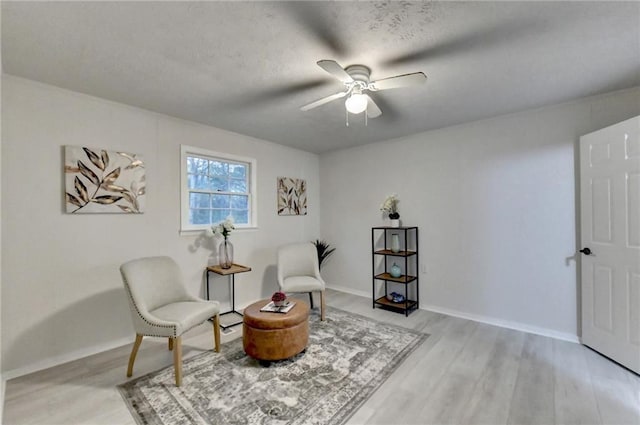 sitting room featuring ceiling fan, light wood finished floors, baseboards, and a textured ceiling