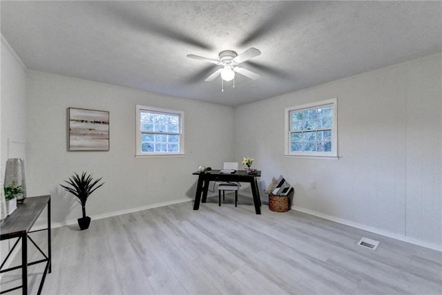 office area with baseboards, a textured ceiling, a ceiling fan, light wood-style floors, and visible vents