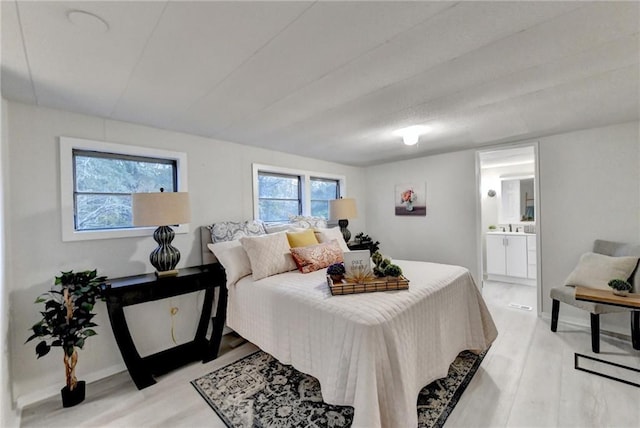 bedroom featuring baseboards, light wood finished floors, and connected bathroom