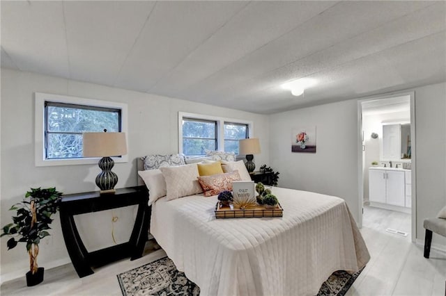 bedroom featuring ensuite bathroom, baseboards, and light wood finished floors
