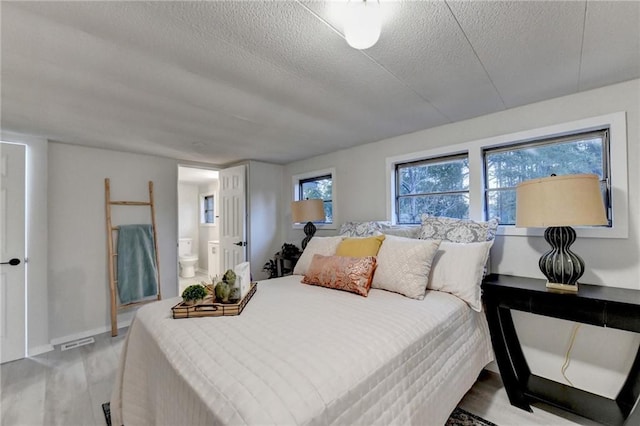 bedroom with connected bathroom, light wood-style flooring, a textured ceiling, visible vents, and baseboards