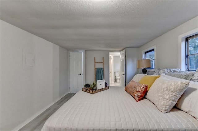 bedroom with ensuite bath, wood finished floors, and a textured ceiling