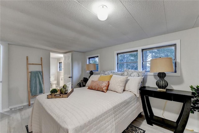bedroom featuring visible vents, ensuite bathroom, wood finished floors, and a textured ceiling