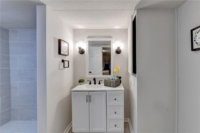 bathroom featuring a tile shower, a textured ceiling, vanity, and baseboards