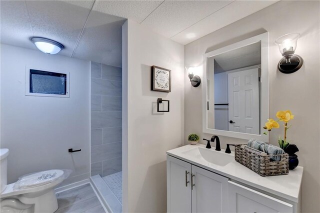 bathroom featuring toilet, tiled shower, vanity, and a textured ceiling