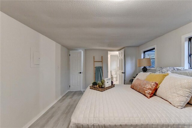 bedroom featuring ensuite bath, light wood-style flooring, a textured ceiling, and baseboards