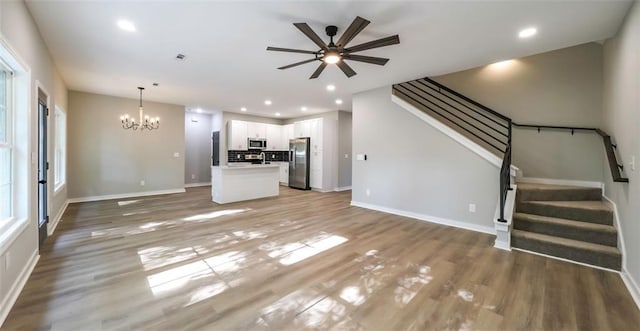 unfurnished living room with recessed lighting, light wood-style floors, stairs, and ceiling fan with notable chandelier