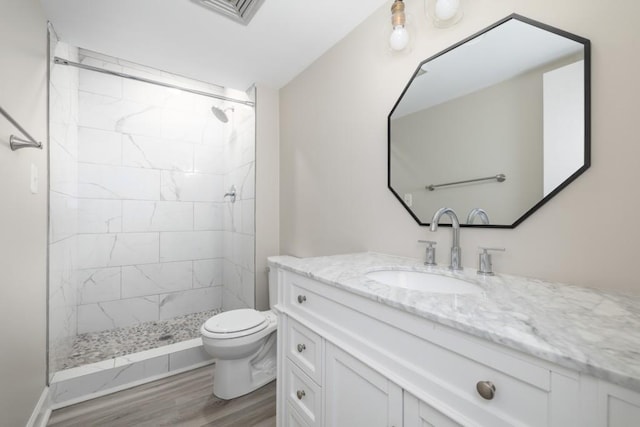 bathroom featuring toilet, hardwood / wood-style floors, tiled shower, and vanity