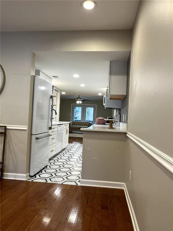 kitchen with ceiling fan, kitchen peninsula, wood-type flooring, white appliances, and white cabinets