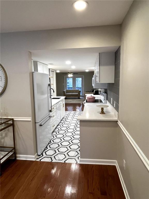 kitchen featuring kitchen peninsula, fridge, white cabinetry, dark wood-type flooring, and range