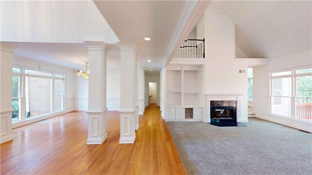 unfurnished living room with built in features, light hardwood / wood-style flooring, a towering ceiling, and plenty of natural light