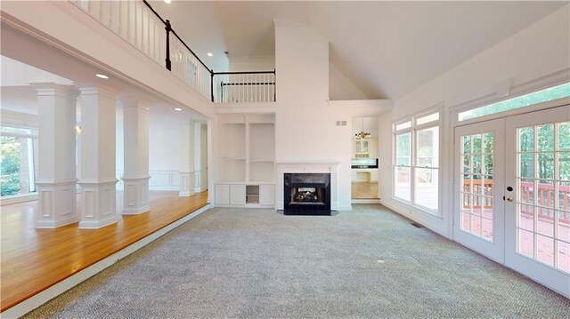 unfurnished living room with french doors, built in features, hardwood / wood-style floors, ornate columns, and a high ceiling