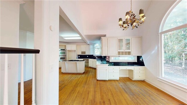 kitchen featuring white cabinetry, stainless steel double oven, light wood-type flooring, and backsplash